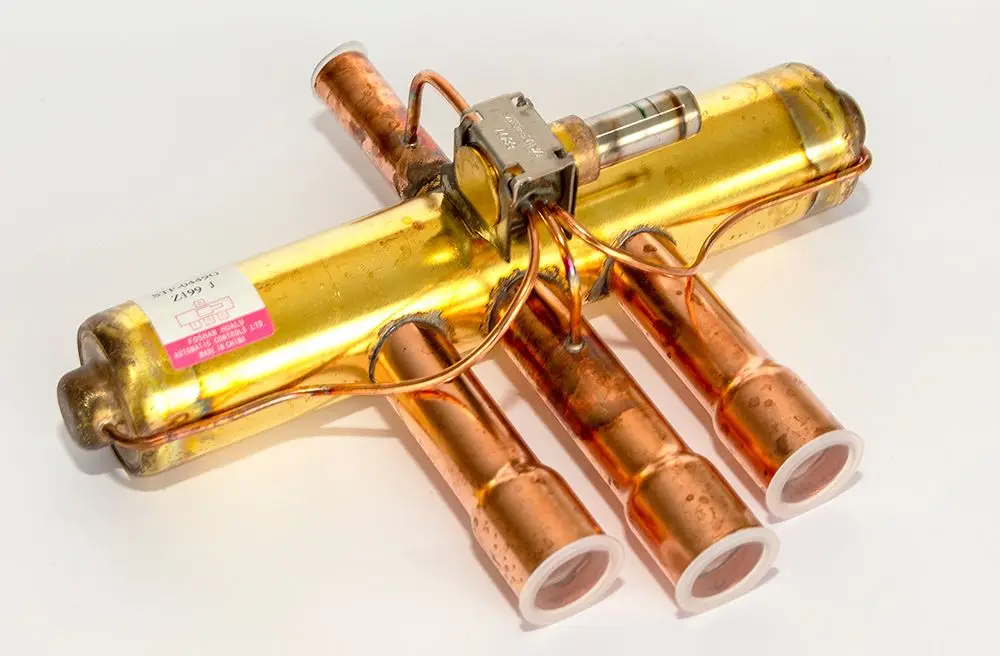 Daikin Ventilkörper mit vier Anschlüssen, metallisch, verbunden durch Rohre. Eignet sich für Heizungsanwendungen, möglicherweise im Bereich der Wärmepumpentechnologie.